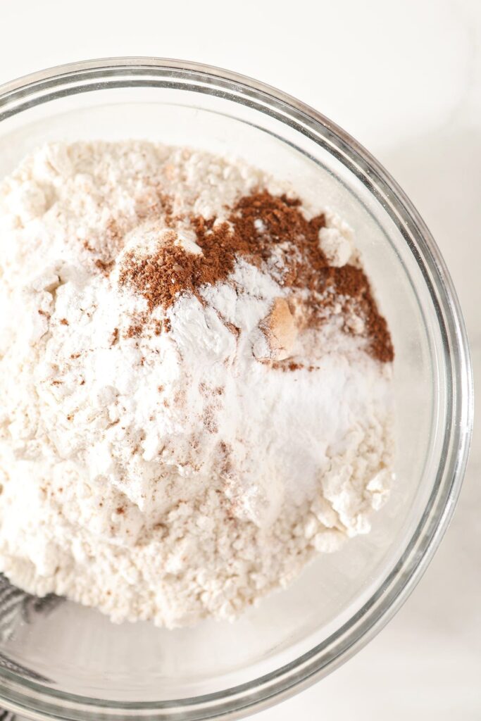 Flour, baking powder, baking soda and ground cinnamon in a glass bowl on marble