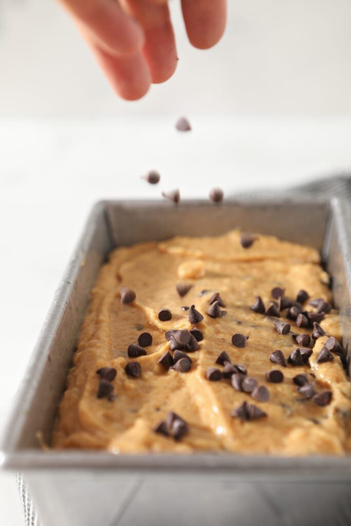 Mini chocolate chips are sprinkled on top of pumpkin bread batter in a loaf pan