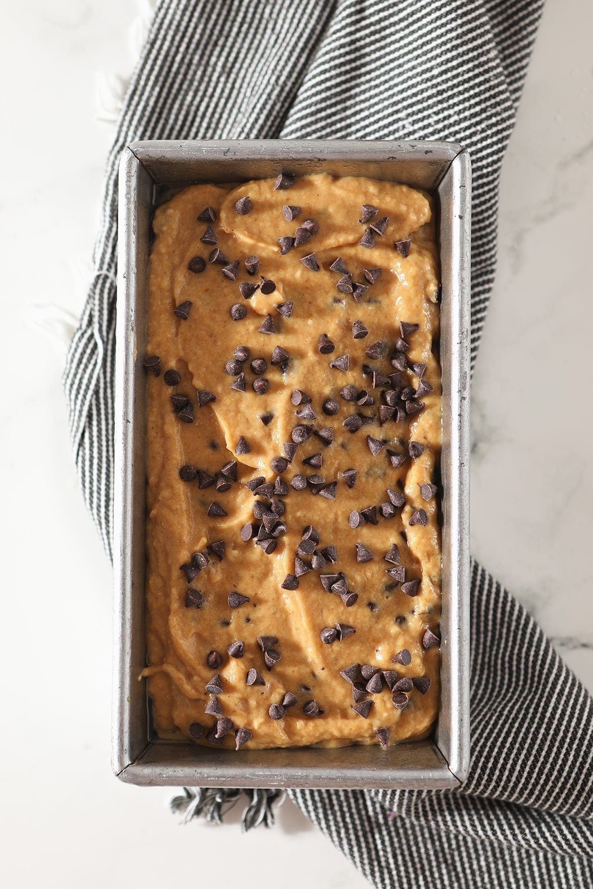 Chocolate Chip Pumpkin Bread batter in a metal pan on top of a gray striped towel, before baking