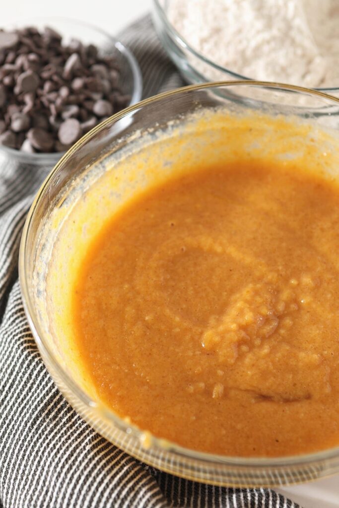 Orange wet ingredients in a glass bowl on a gray towel