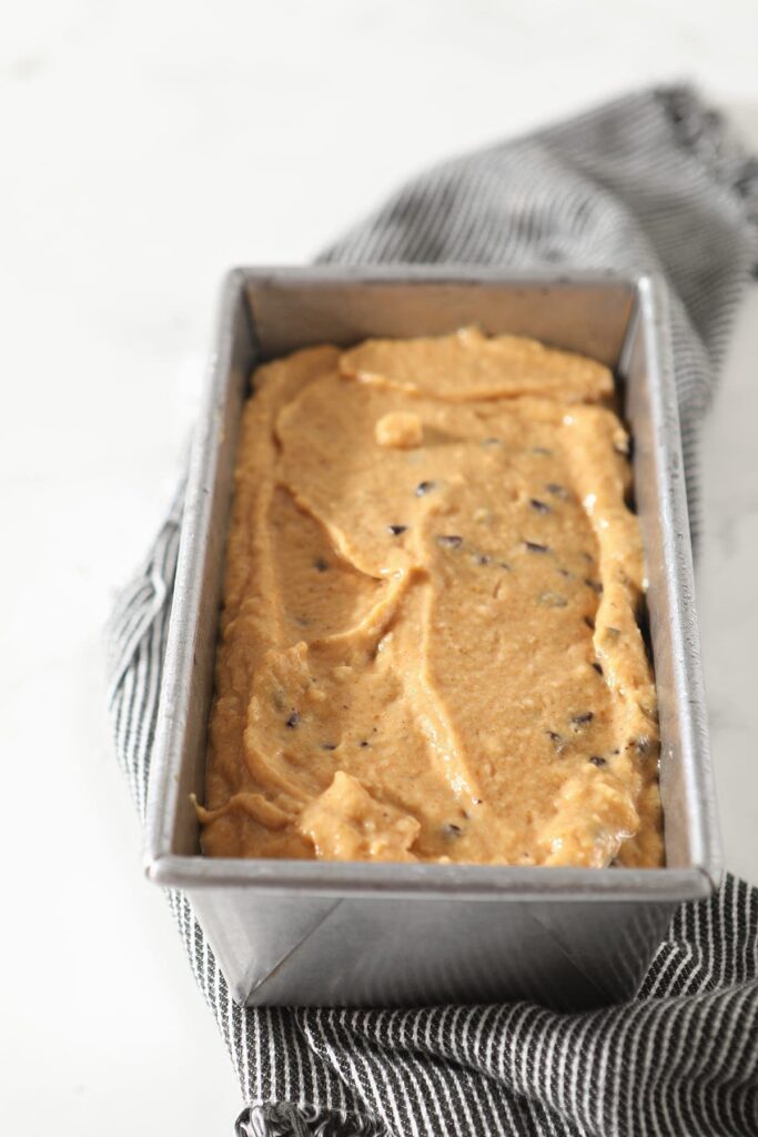 Pumpkin bread batter in a loaf pan on a gray striped towel