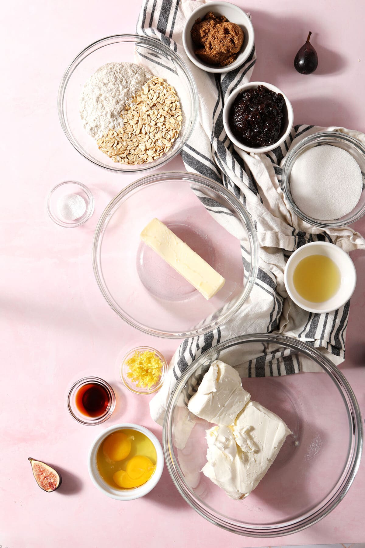 bowls of ingredients to make cheesecake bars with lemon and figs on a pink surface with a white and grey striped linen
