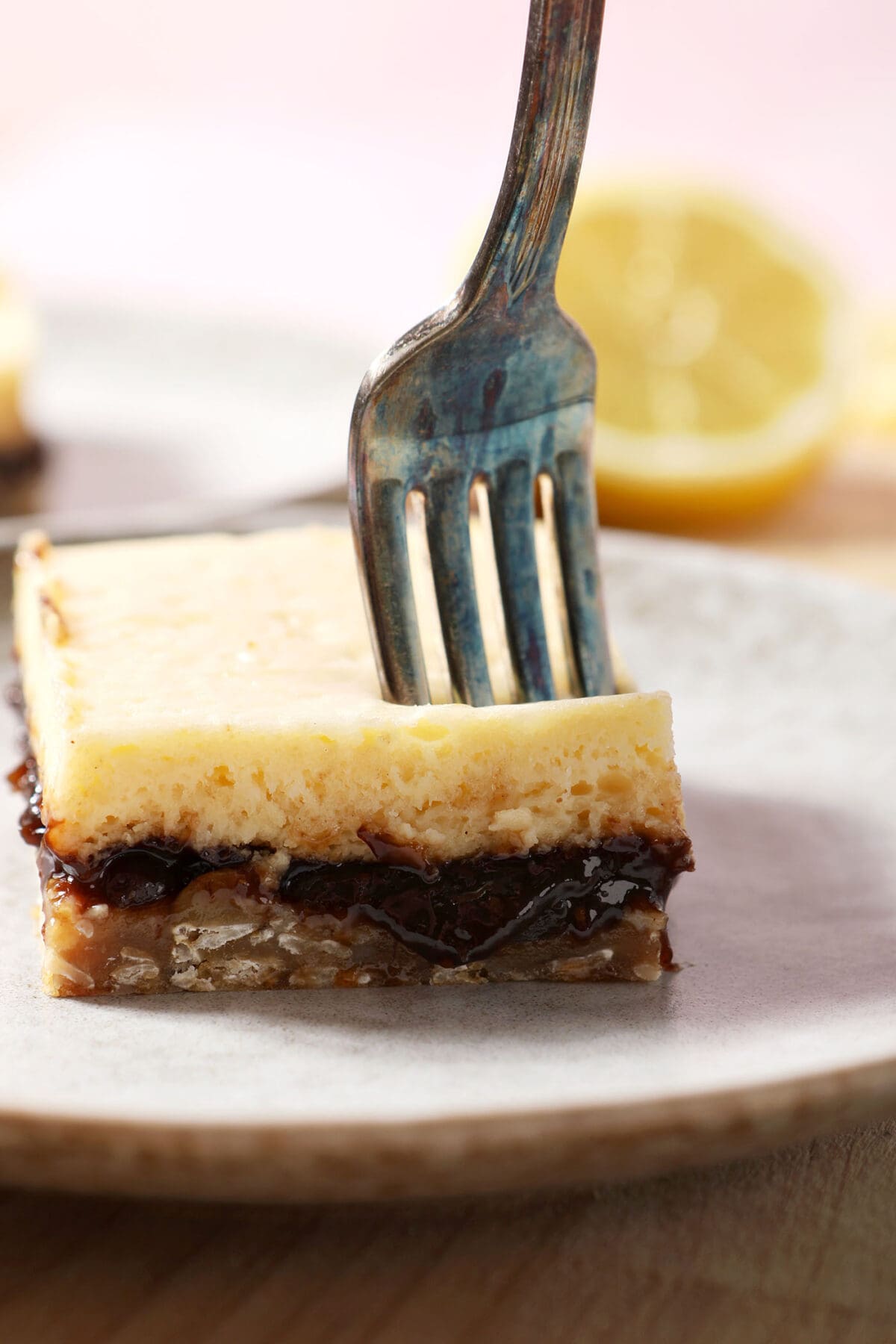 a fork cuts into a cheesecake bar with fig and lemon on a white plate