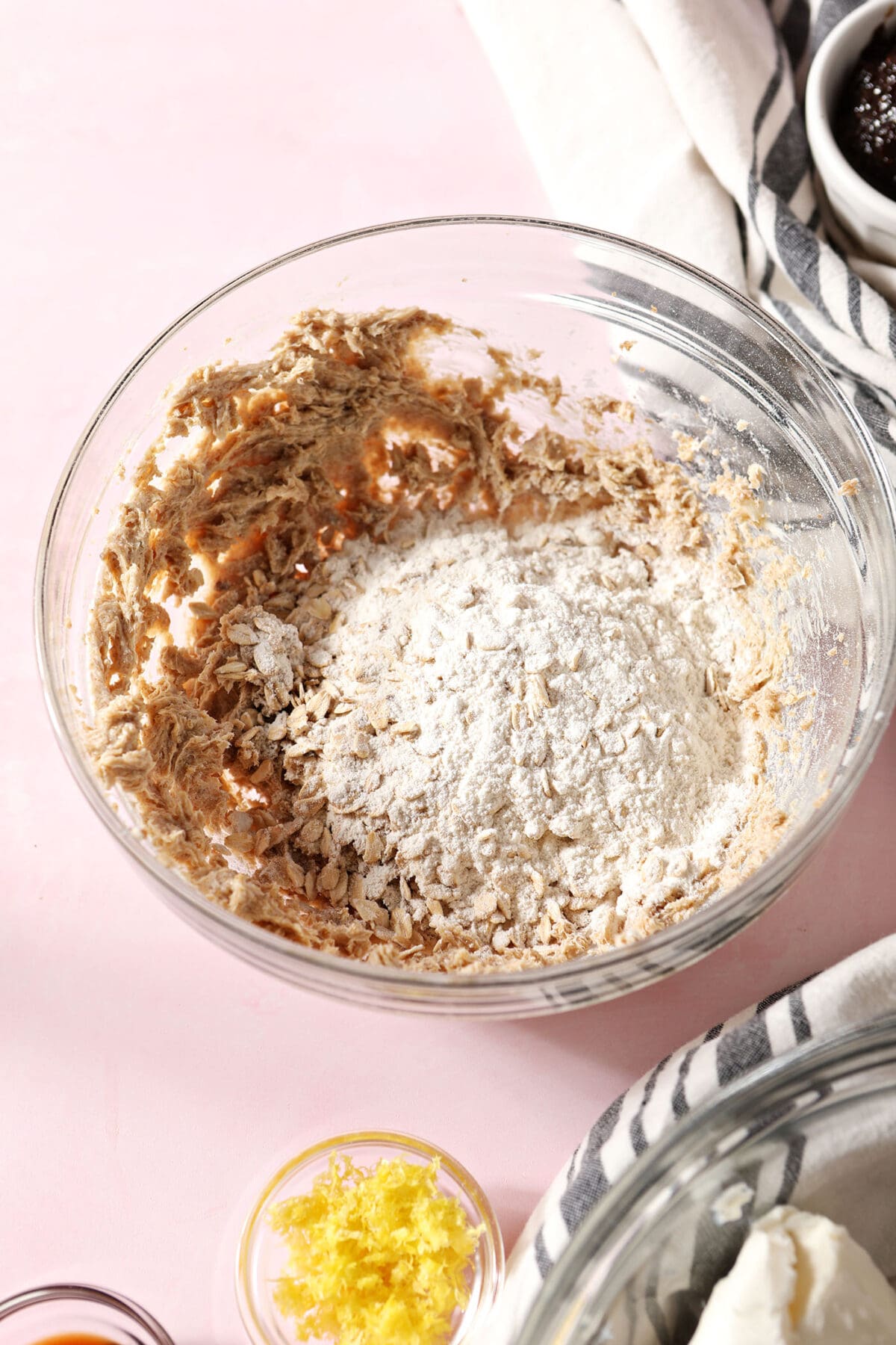oats, flour and salt sit on top of creamed butter and sugar in a bowl on a pink surface
