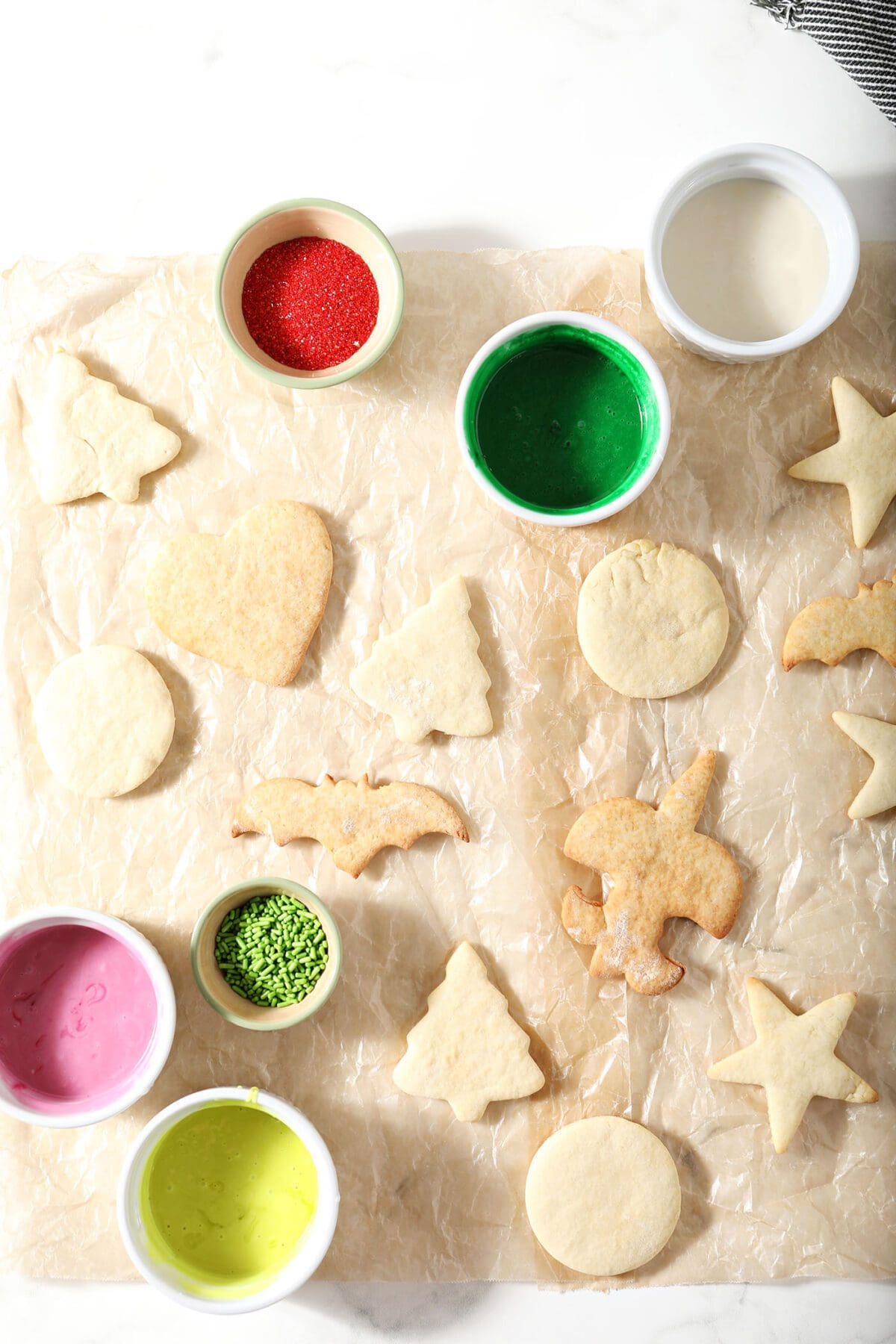 Several cut out sugar cookies on parchment with icing and sprinkles before icing