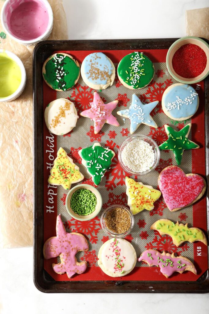 Iced cut out sugar cookies on a silpat-lined sheet pan surrounded with frosting