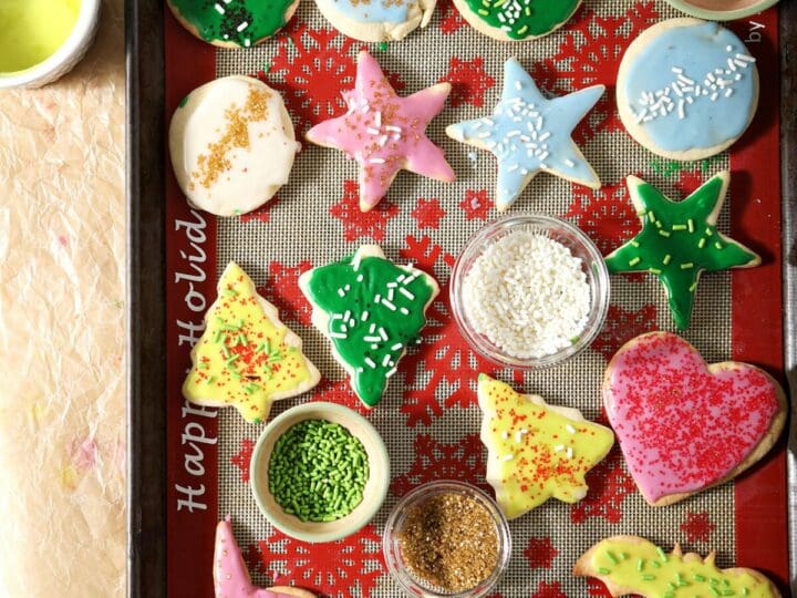 Iced cut out sugar cookies on a silpat-lined sheet pan surrounded with frosting