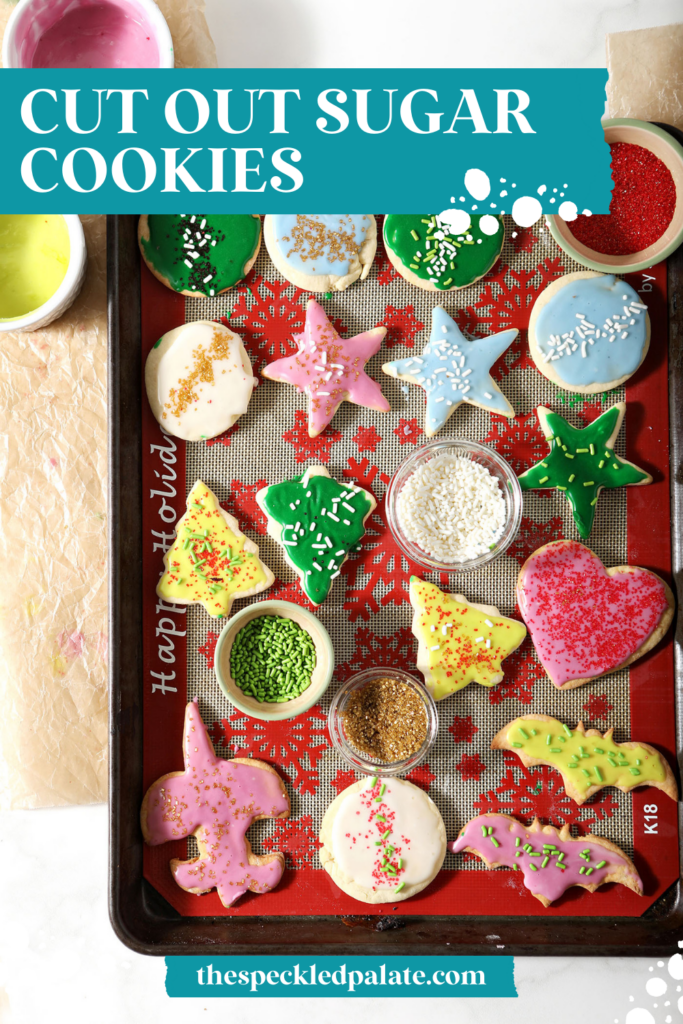 Iced sugar cookies on a silpat-lined sheet pan surrounded with frosting with the text Cut Out Sugar Cookies