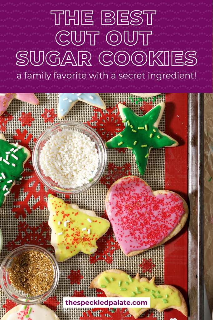 Iced sugar cookies in various shapes on a silpat-lined sheet pan with the text The Best Cut Out Sugar Cookies a family favorite with a secret ingredient