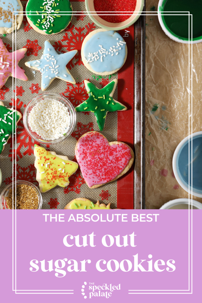 Iced sugar cookies on a silpat-lined sheet pan surrounded with frosting with the text The Absolute Best Cut Out Sugar Cookies