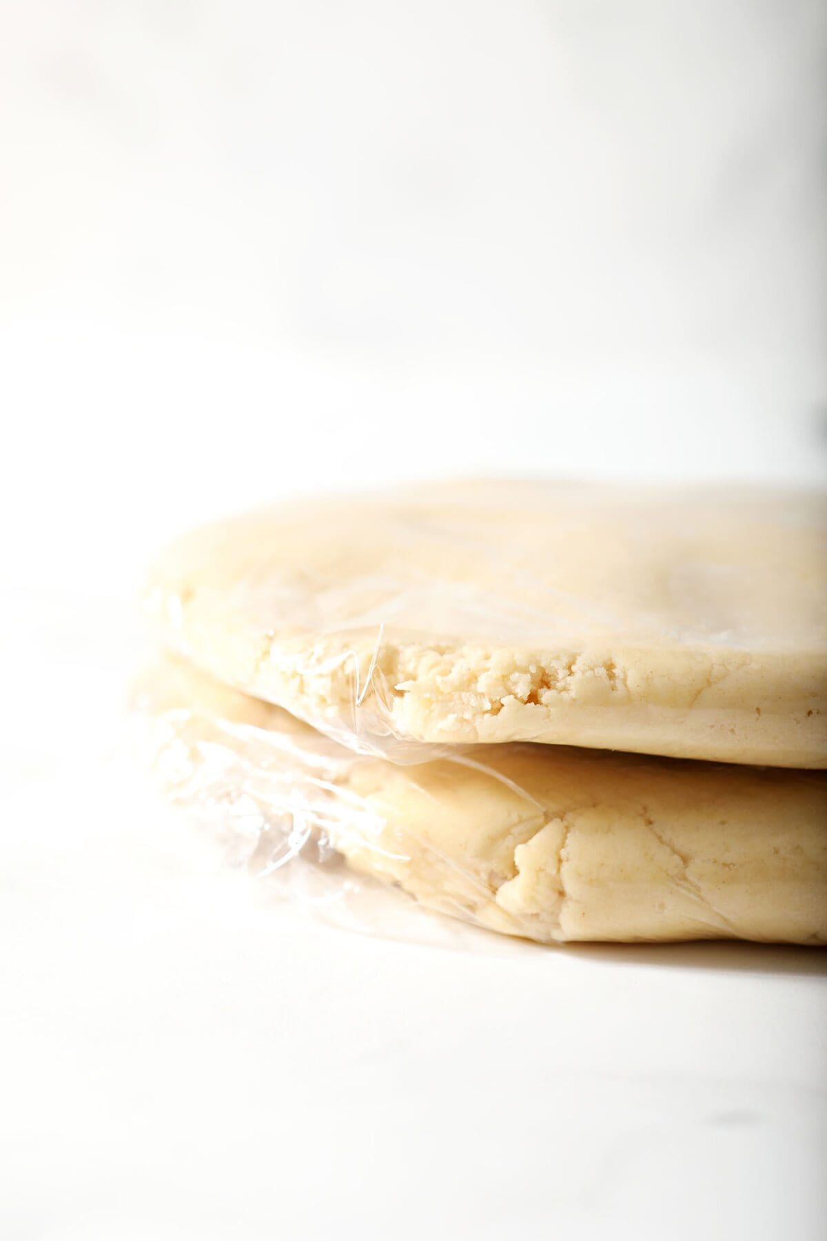 Two rounds of cut out sugar cookie dough in plastic wrap before chilling