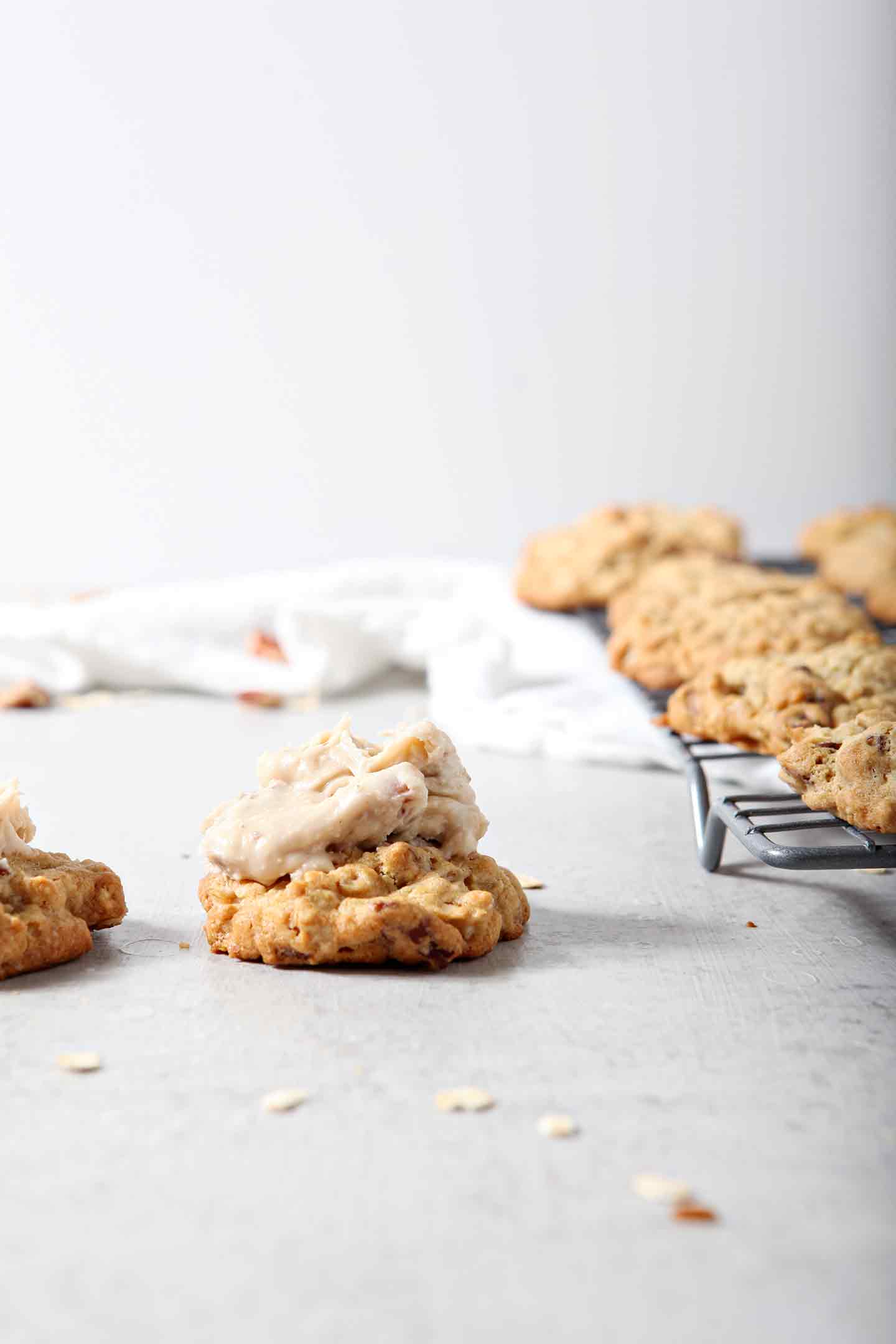 Two iced Quebec Maple Pecan Drop Cookies sit beside a wire cooling rack holding the cookies.