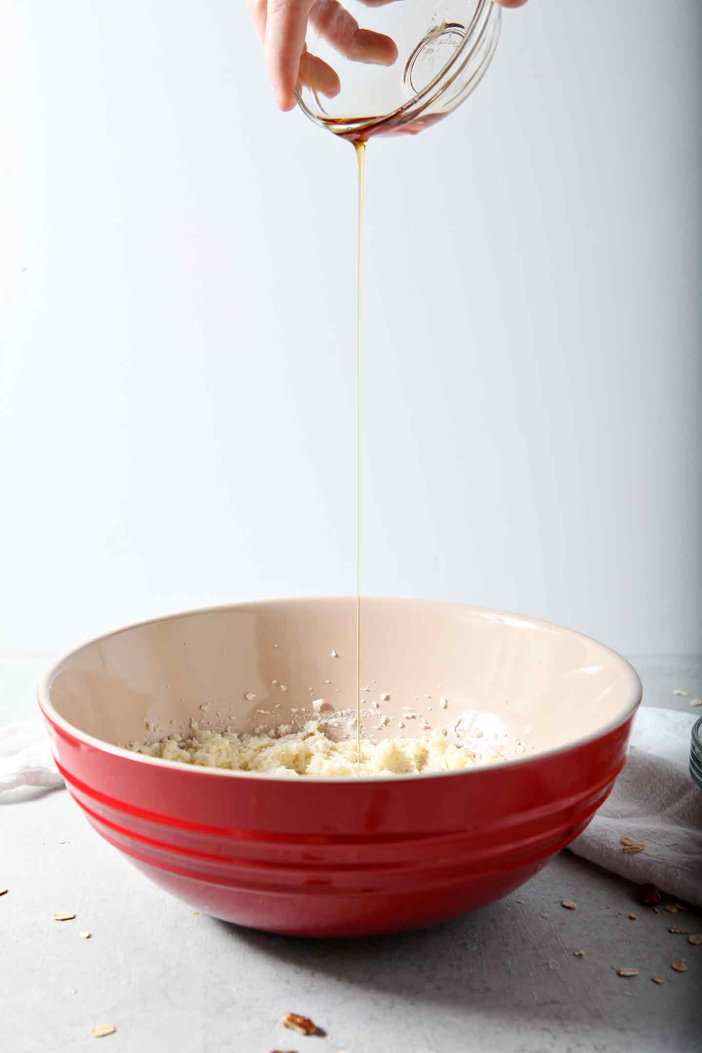 Maple syrup is drizzled into the wet ingredients for Quebec Maple Pecan Drop Cookies, which are held in a red bowl