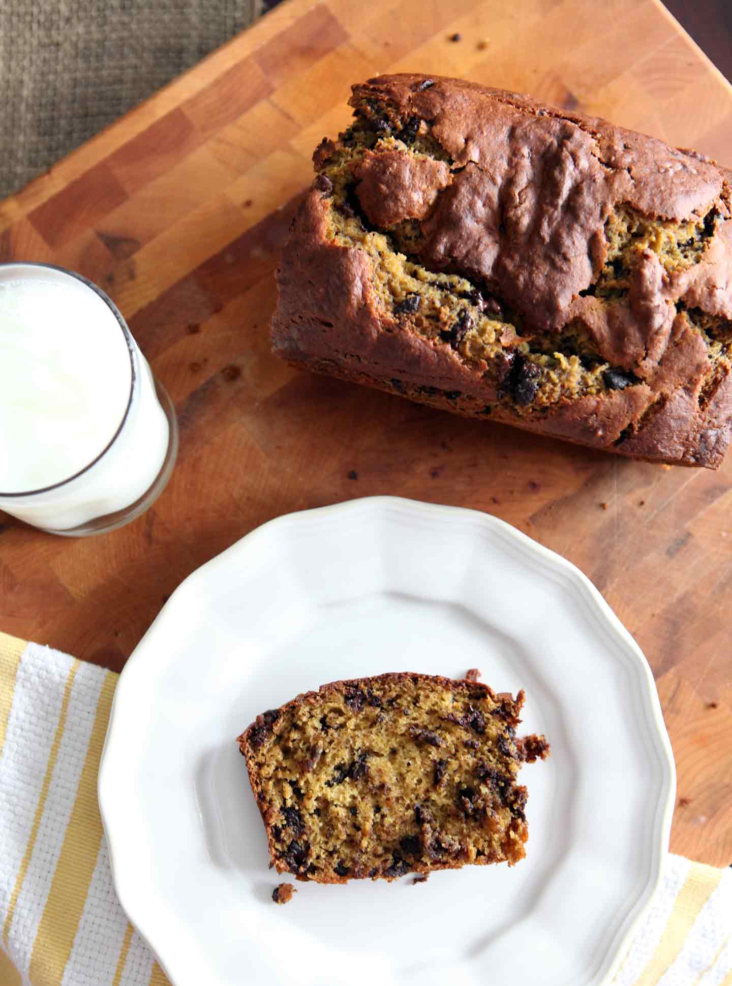 Overhead of a slice of Chocolate Chip Pumpkin Bread on a white platter next to a loaf and a glass of milk