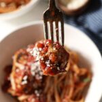 A fork spears a meatball over a bowl of pasta