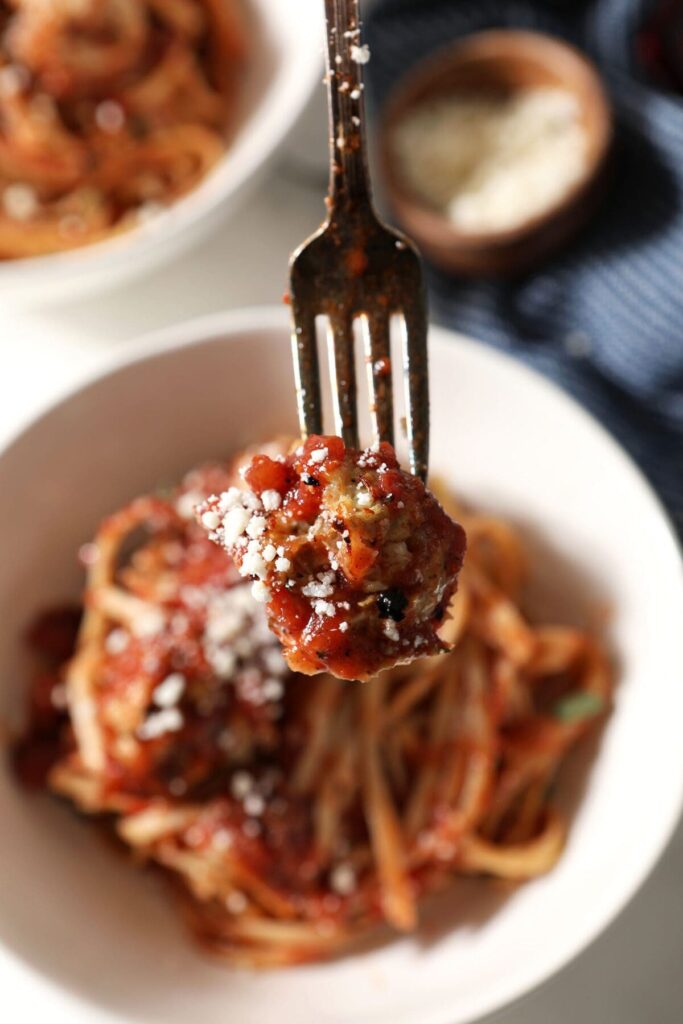 A fork spears a meatball over a bowl of pasta