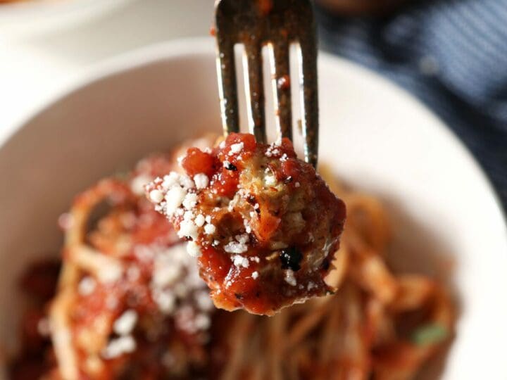 A fork spears a meatball over a bowl of pasta