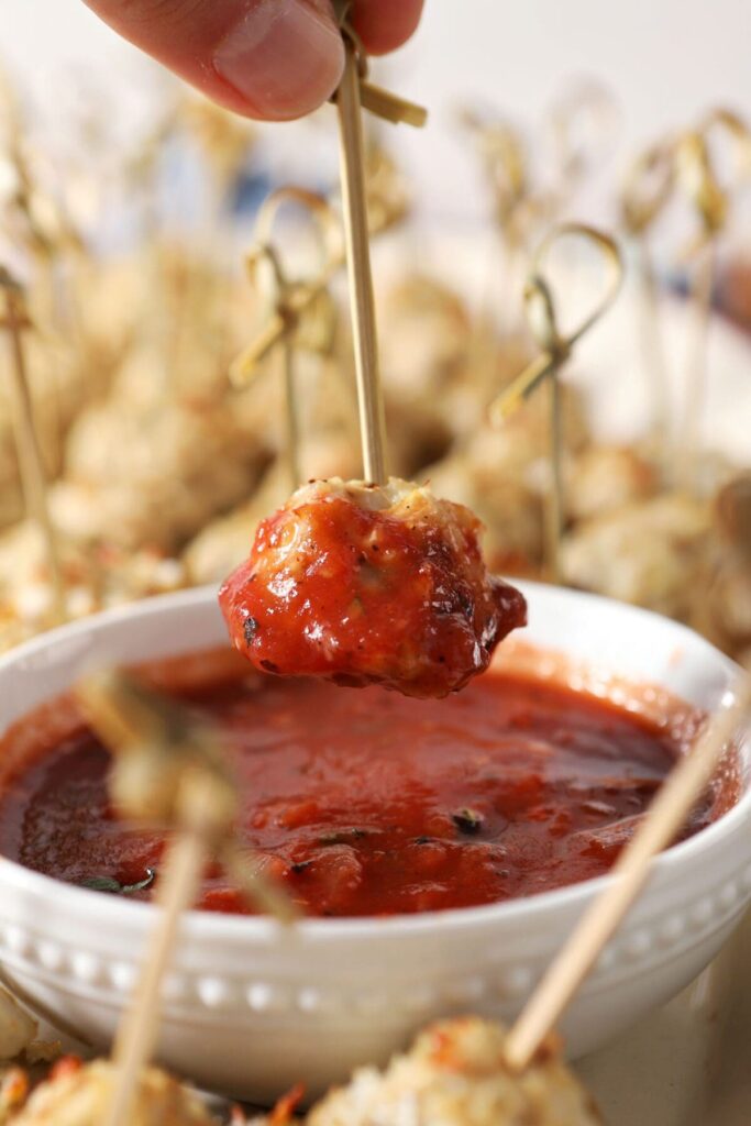 A meatballs dips into a bowl of marinara