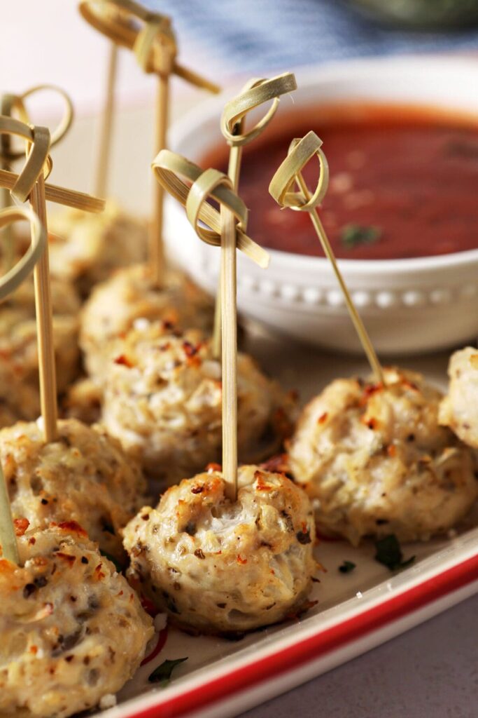 Skewered turkey meatballs on a platter next to homemade marinara sauce