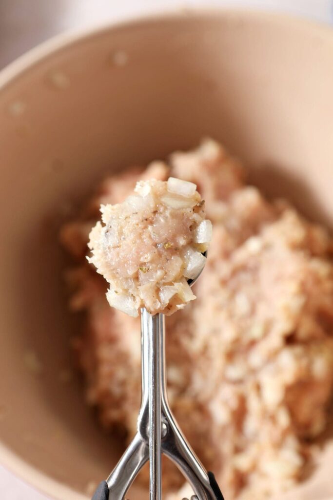 A cookie scoop over a bowl of turkey meatball meat