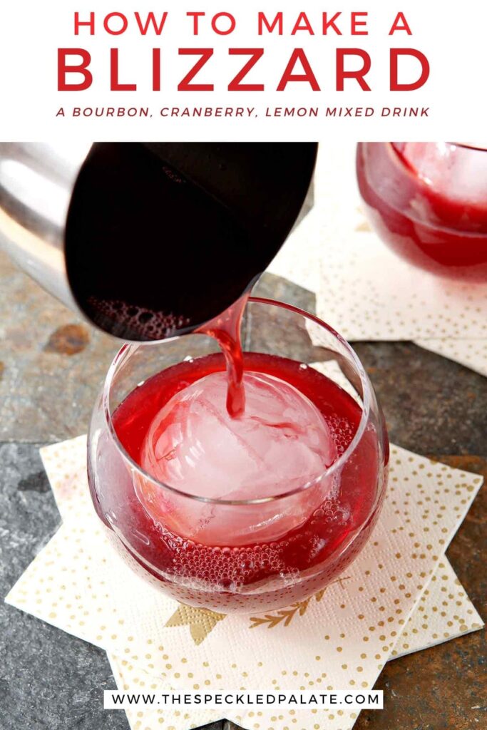 A silver cocktail shaker pours red liquid into an old fashioned glass with a large spherical ice cube with the text 'how to make a blizzard. a bourbon, cranberry, lemon mixed drink.'