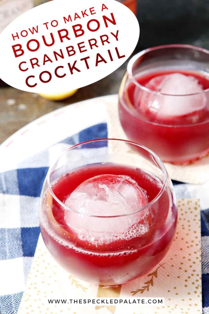 Two red drinks in old fashioned glasses with large spherical ice cubes sit on a blue and white buffalo check napkin with the text 'how to make a bourbon cranberry cocktail'