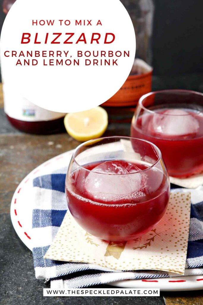 Two red drinks in old fashioned glasses with large spherical ice cubes sit on a blue and white buffalo check napkin with the text 'how to mix a blizzard: cranberry, bourbon and lemon drink'