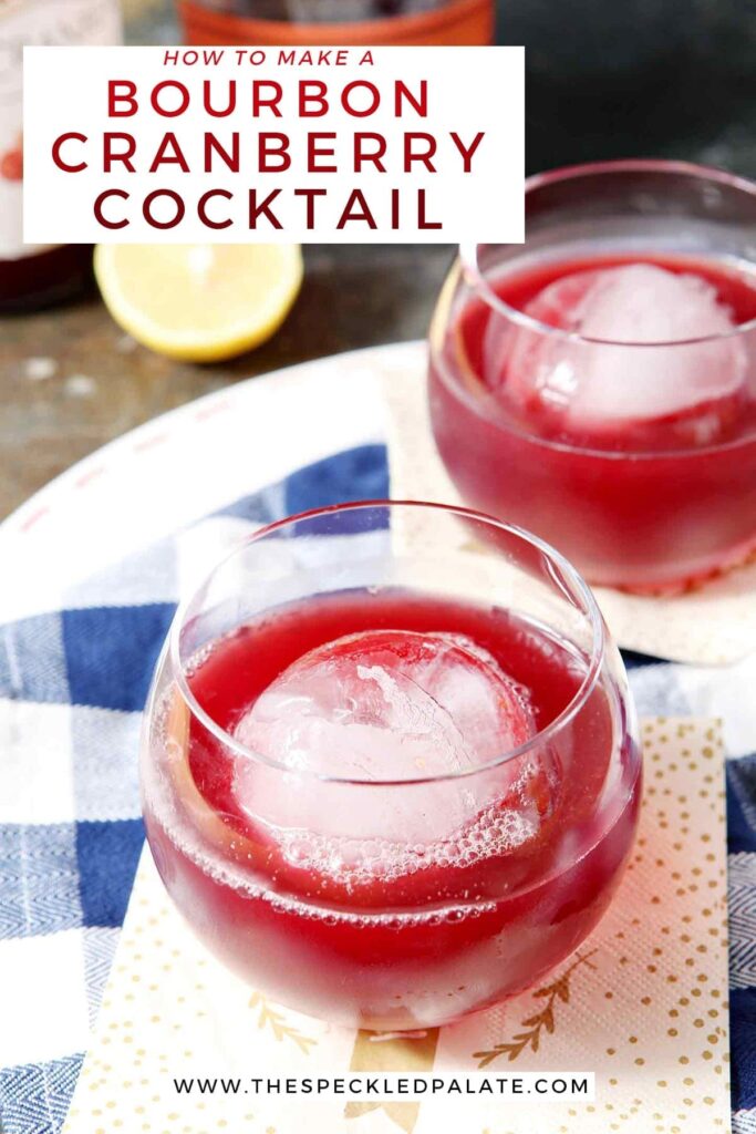 Two red drinks in old fashioned glasses with large spherical ice cubes sit on a blue and white buffalo check napkin with the text 'how to make a bourbon cranberry cocktail'