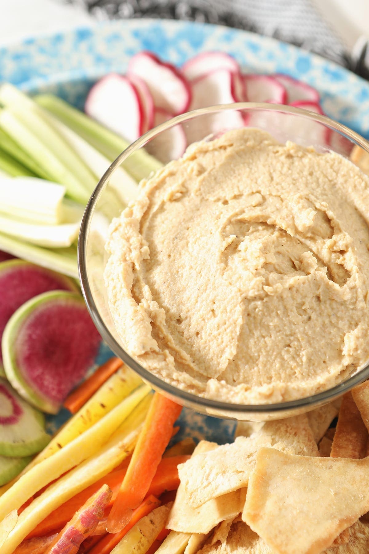 Close up of hummus dip in a clear glass bowl surrounded by veggie slices