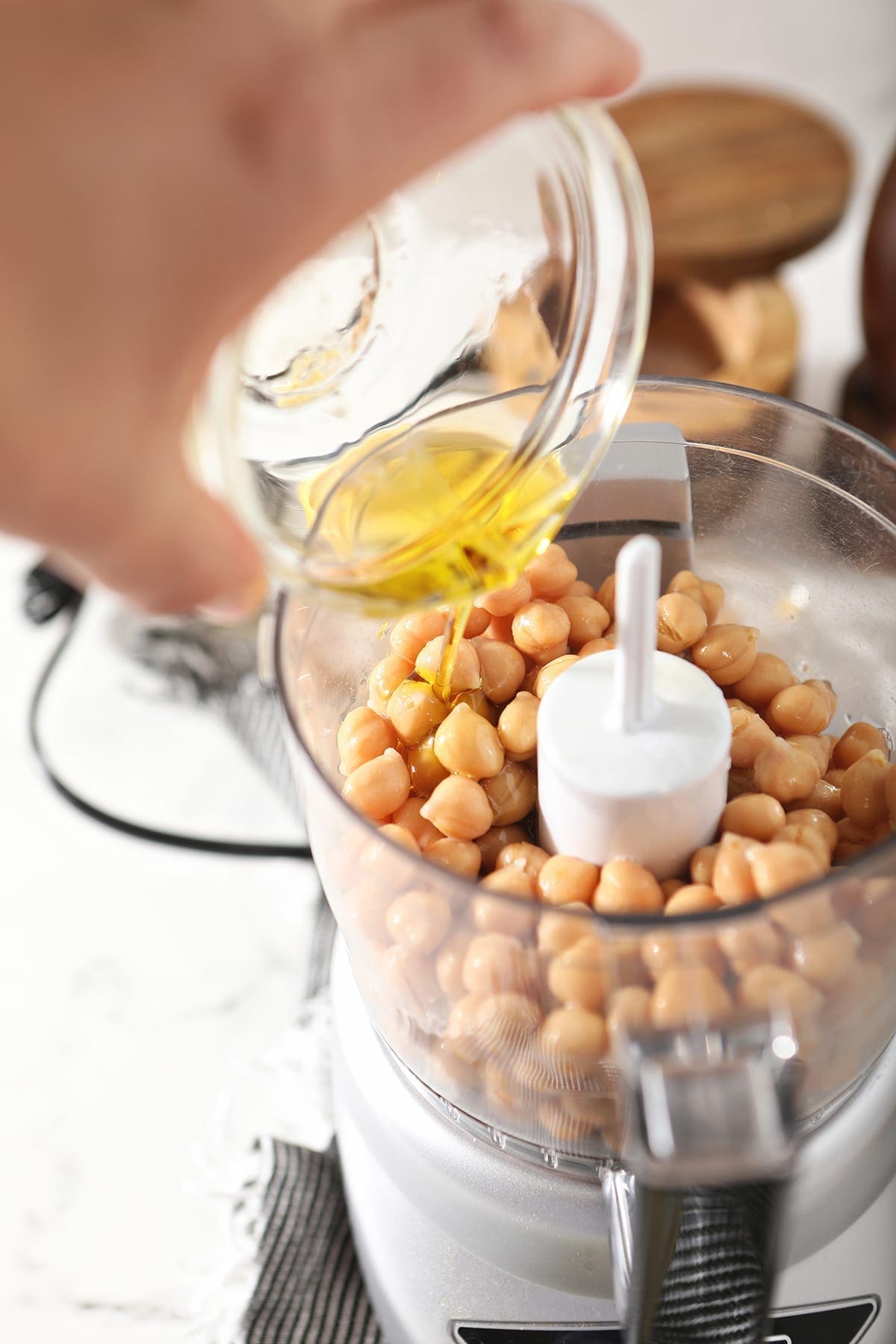 Olive oil is poured into a food processor with chickpeas already in it