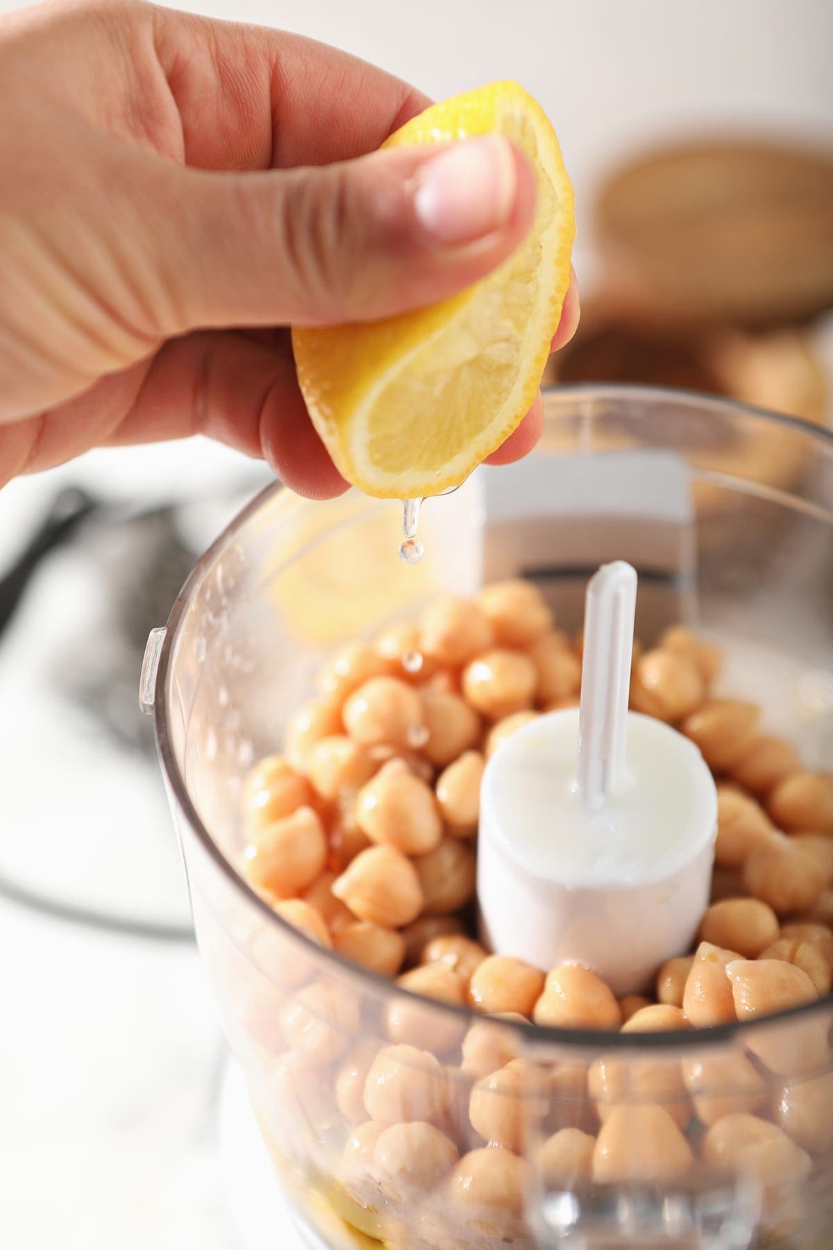 A lemon is squeezed on top of chickpeas and other ingredients in a food processor