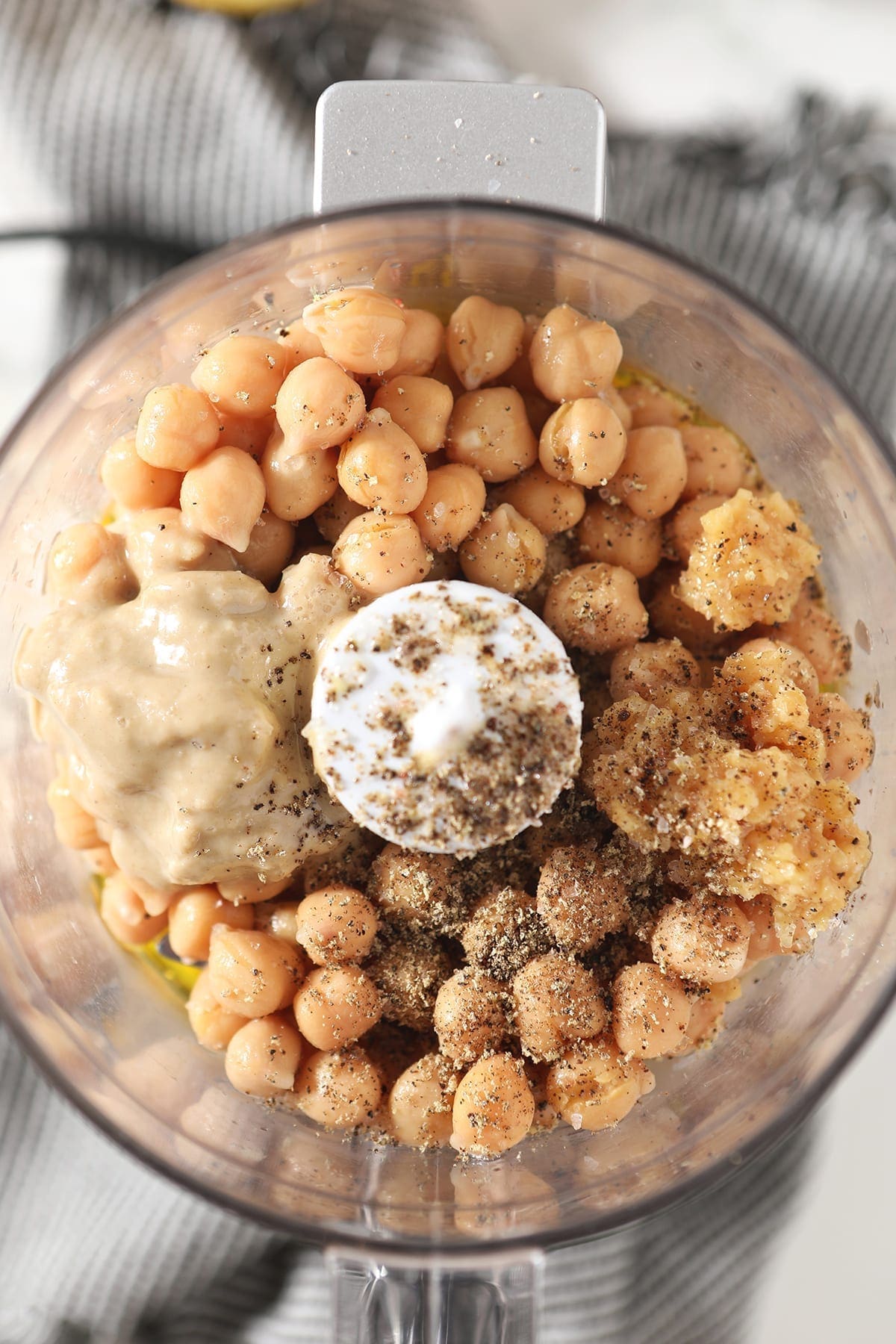 Close up of chickpeas, salt, pepper, tahini, garlic and other ingredients in a food processor before blending