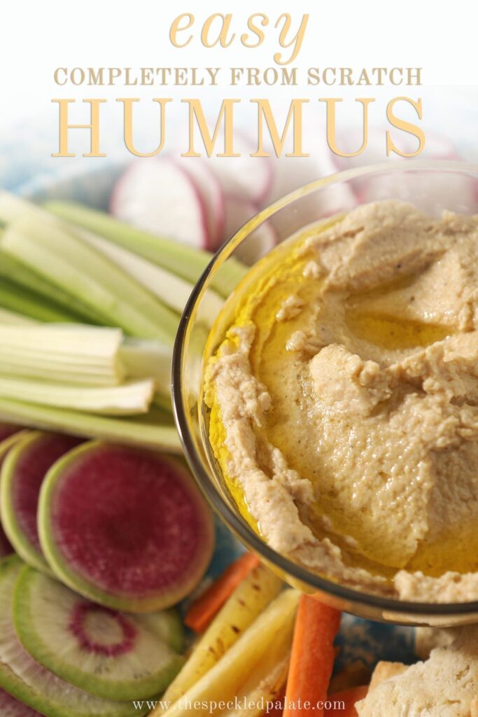 Close up of a bowl of hummus, drizzled with olive oil, surrounded by veggies for dipping with the text "Easy completely from scratch hummus"