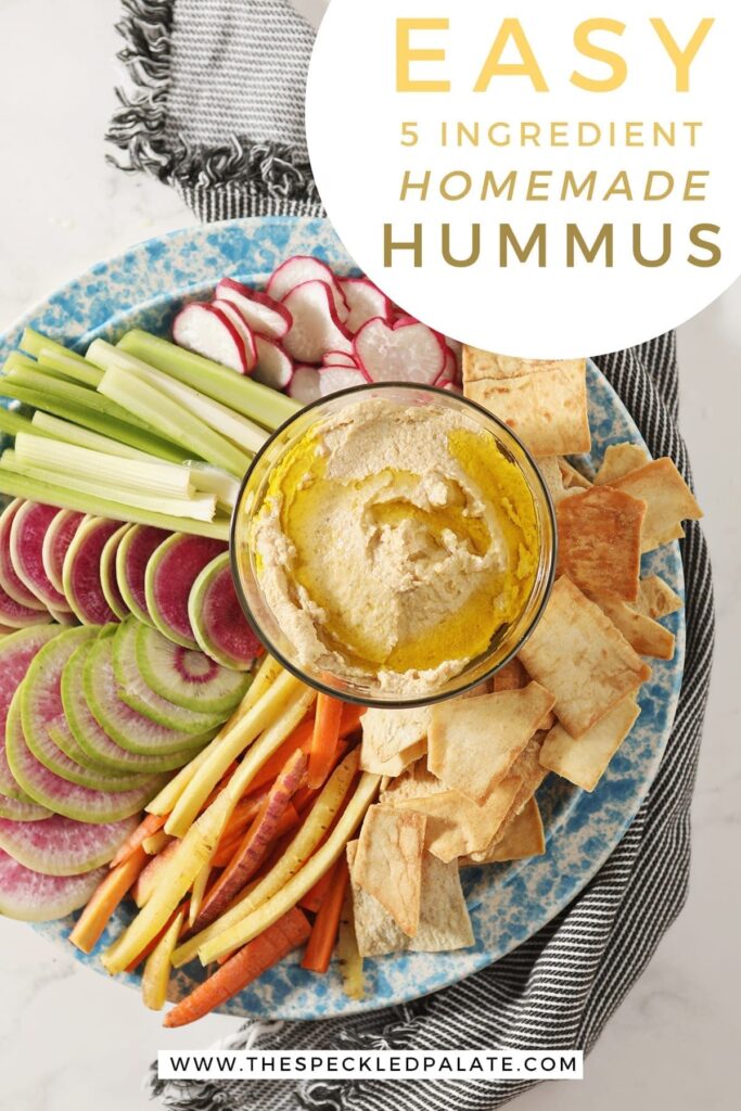 Hummus, drizzled with olive oil, sits in a glass container surrounded by radish, celery and carrot slices and pita chips with text "Easy 5-ingredient homemade hummus"