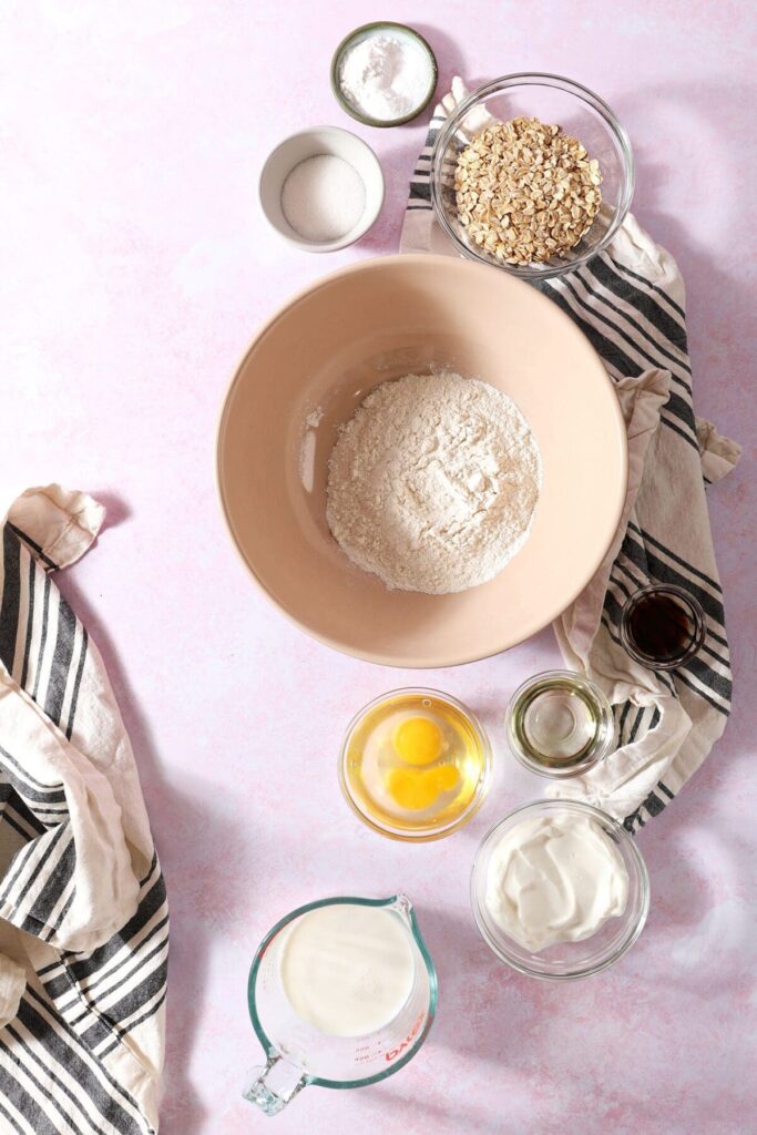 Ingredients to make oat flour pancakes in bowls on a pink countertop