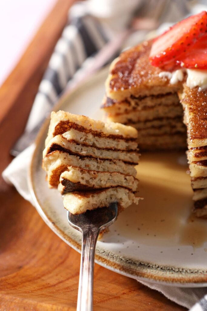 A fork holds a large bite of sliced oat flour pancakes next to a stack