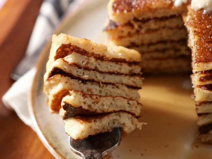 A fork holds a large bite of sliced oat flour pancakes next to a stack