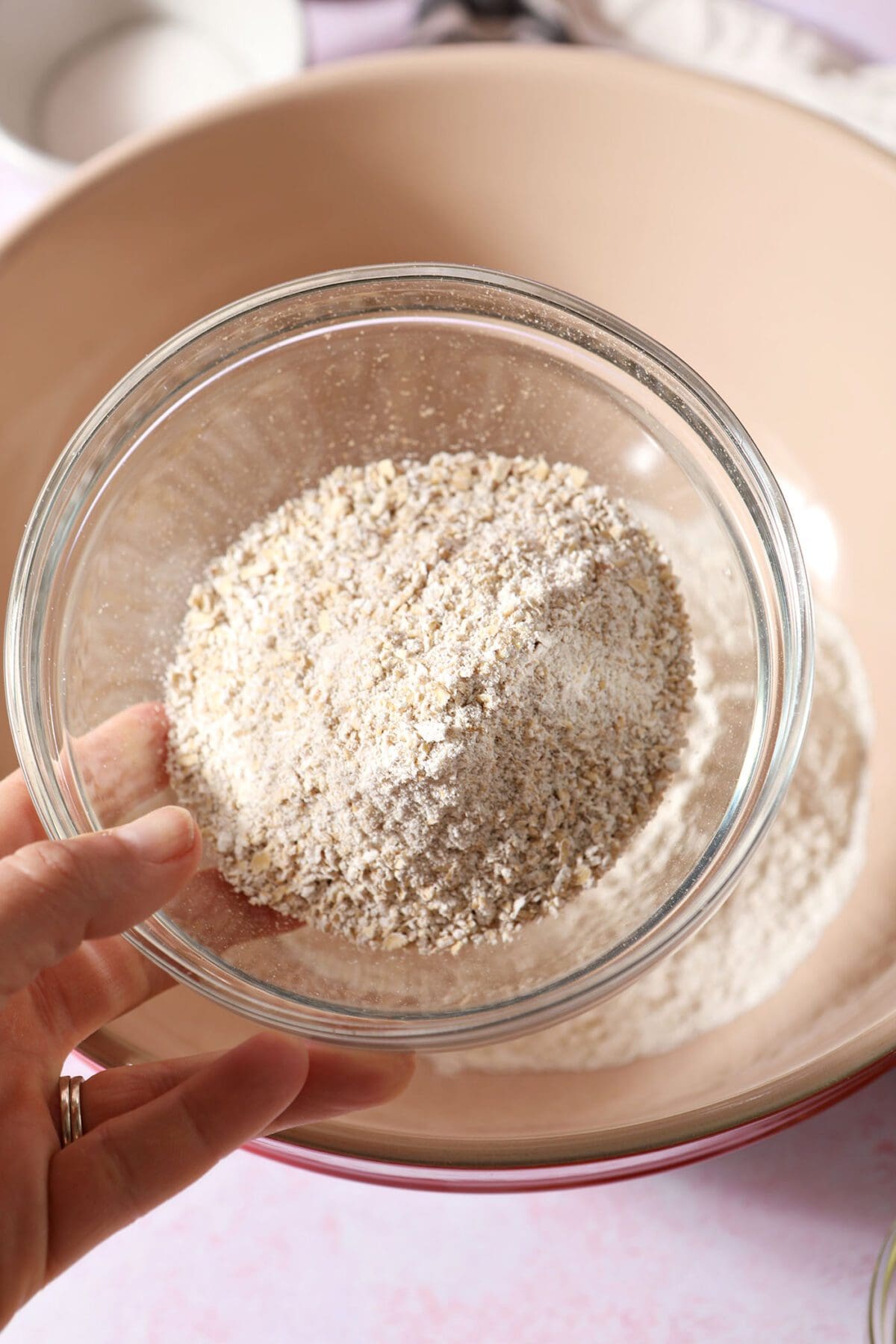 A person holds a bowl of homemade oat flour above another bowl