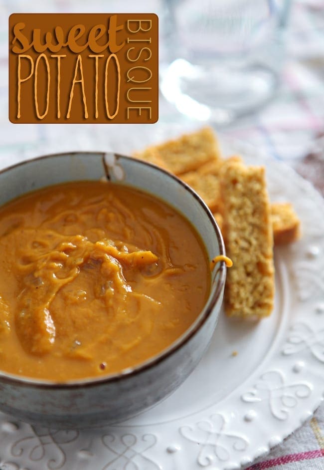 A close up of a bowl holding an orange soup on a white plate with cornbread biscotti next to it on a white plate