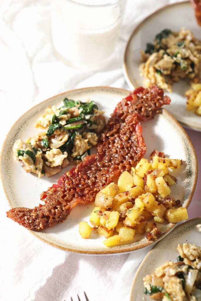 Three plates hold candied bacon with homemade home fries and veggie scrambled eggs