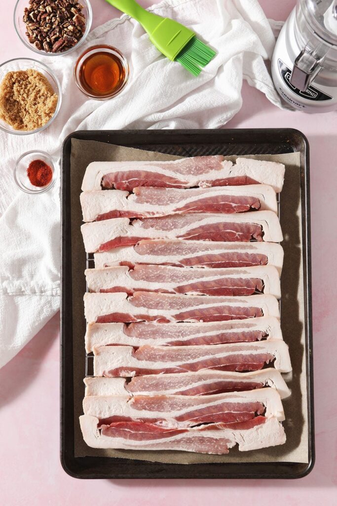 Ingredients for Praline Bacon sit on a baking sheet and in bowls next to it