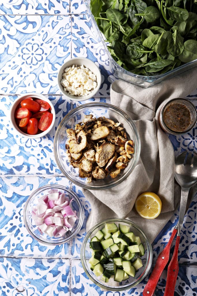 Overhead image of ingredients to make shawarma chicken salad in bowls on a blue and white tiled surface