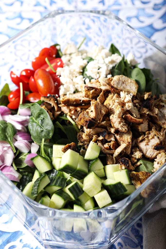 Overhead of a bowl of chicken shawarma salad before mixing on a blue and white tiled surface