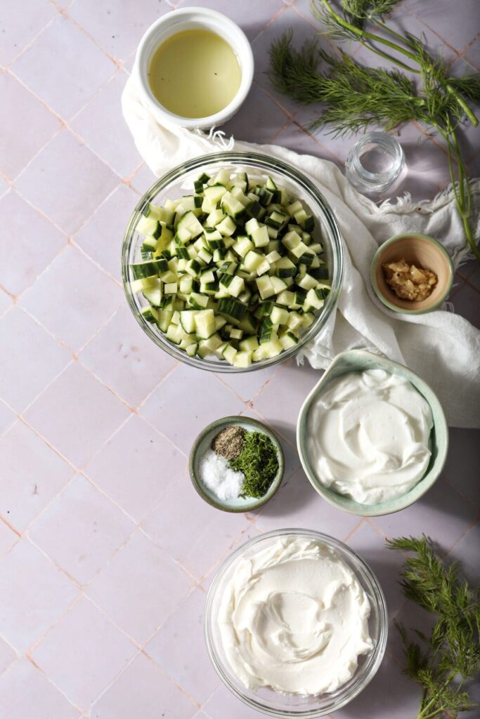 Ingredients to make homemade tzatziki sauce in bowls on a purple countertop