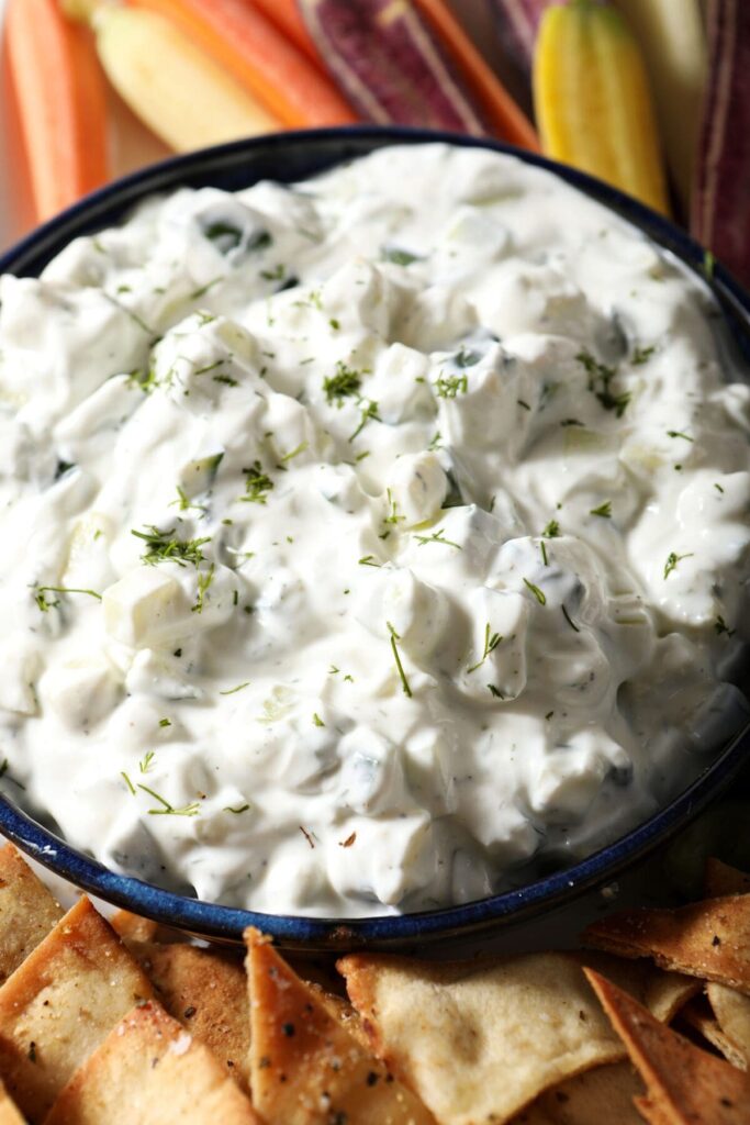 Close up of a bowl of tzatziki sauce surrounded by carrot slivers and pita chips