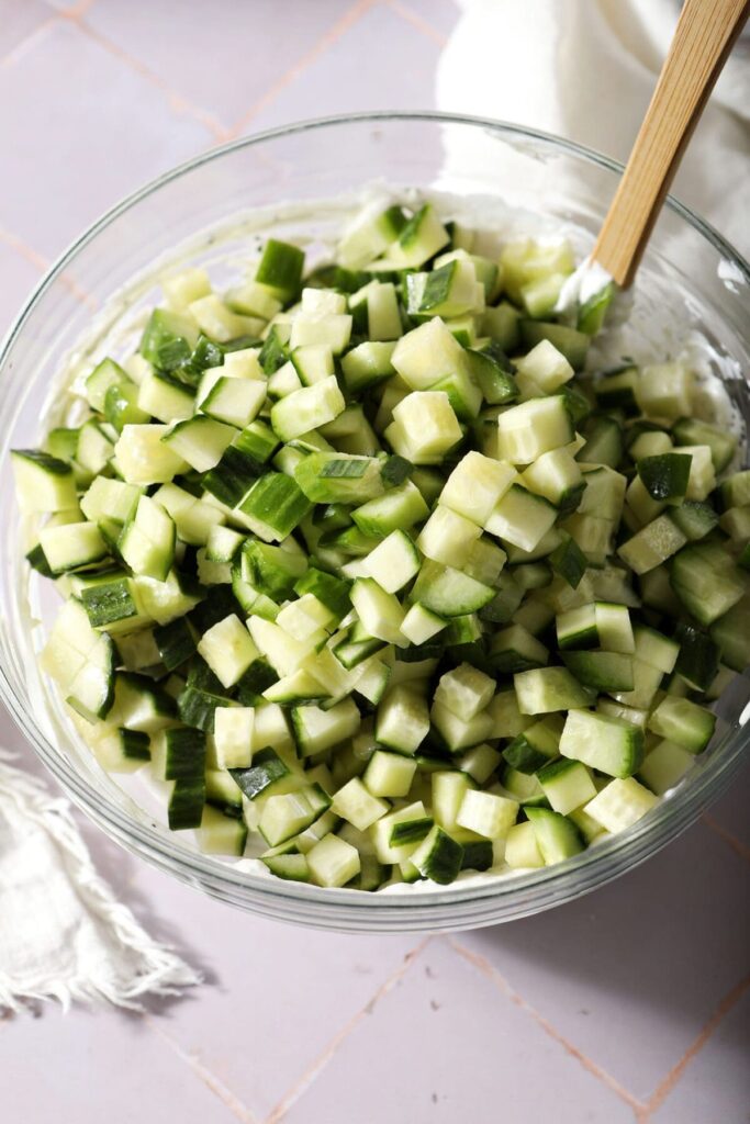 Diced cucumber on top of a bowl of tzatziki sauce