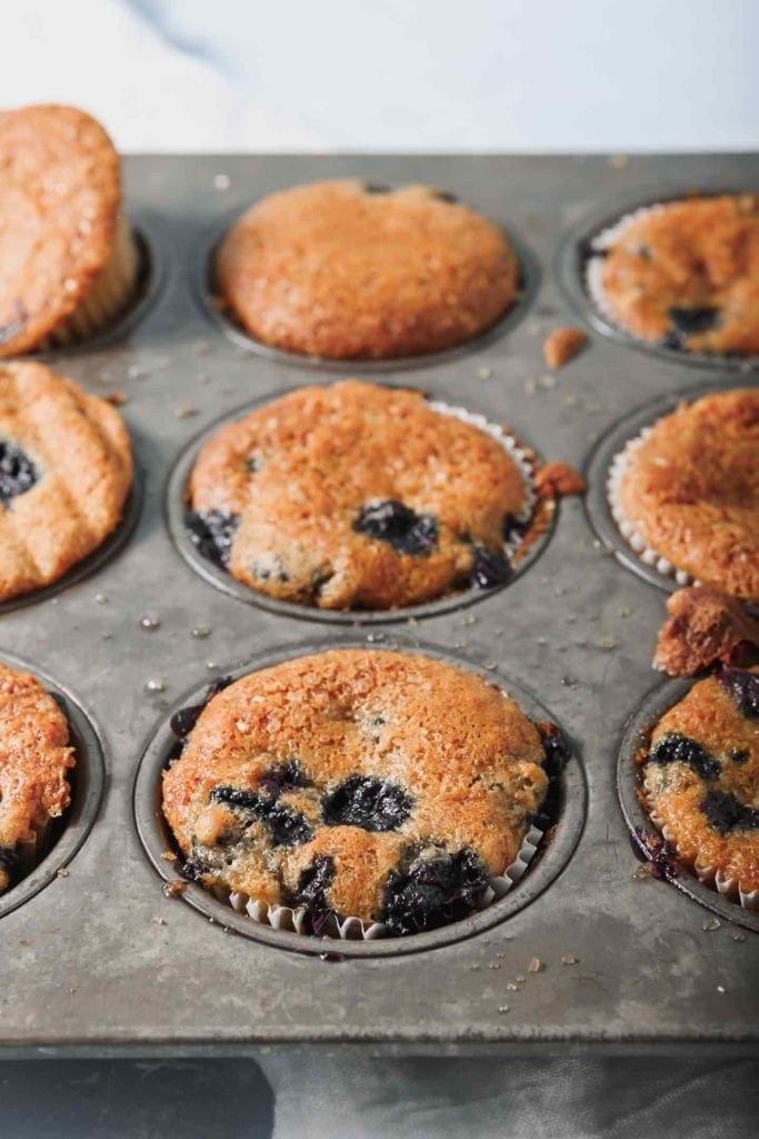 Vegan Blueberry Muffins, in a muffin tin, immediately after baking on a turquoise background.