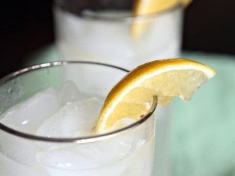 Two silver-lined glasses with Tom Collins are garnished with lemon wedges