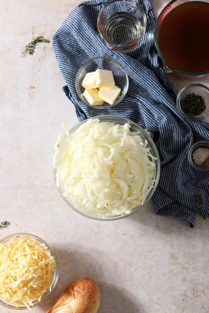 A bowl of onions with other French Onion Soup ingredients with a blue striped towel