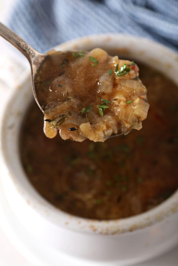 A spoon holds a bite of French Onion Soup over a bowl